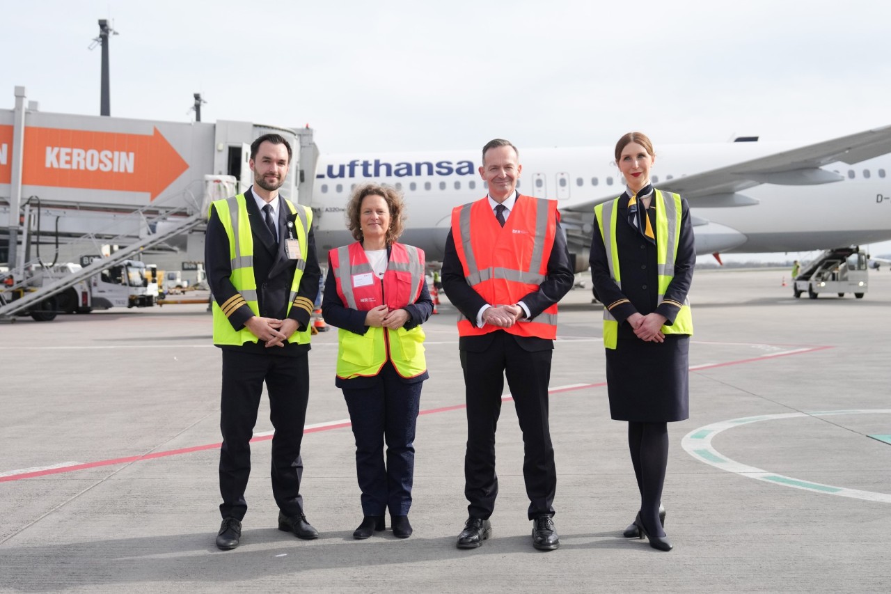 Two women and two men are standing in front of a Lufthansa aircraft. All four are wearing a red or yellow high-visibility waistcoat. They smile friendly into the camera.