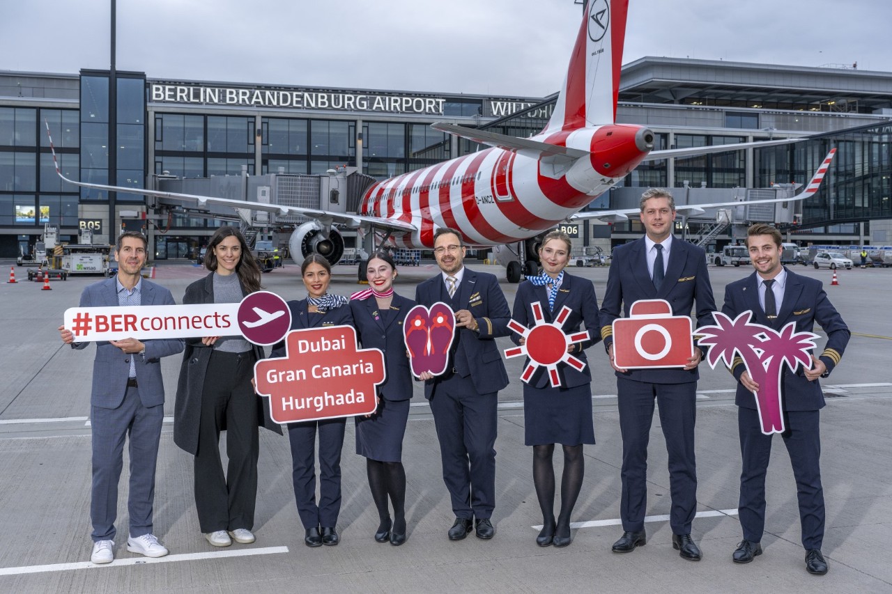 A group of people pose with signs on the apron in front of an aircraft.