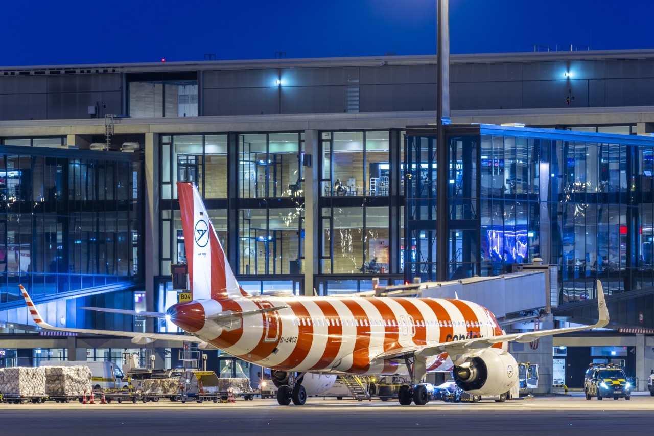 A red and white striped Condor aircraft stands at a ground handling position in front of the BER terminal, which is illuminated at night.