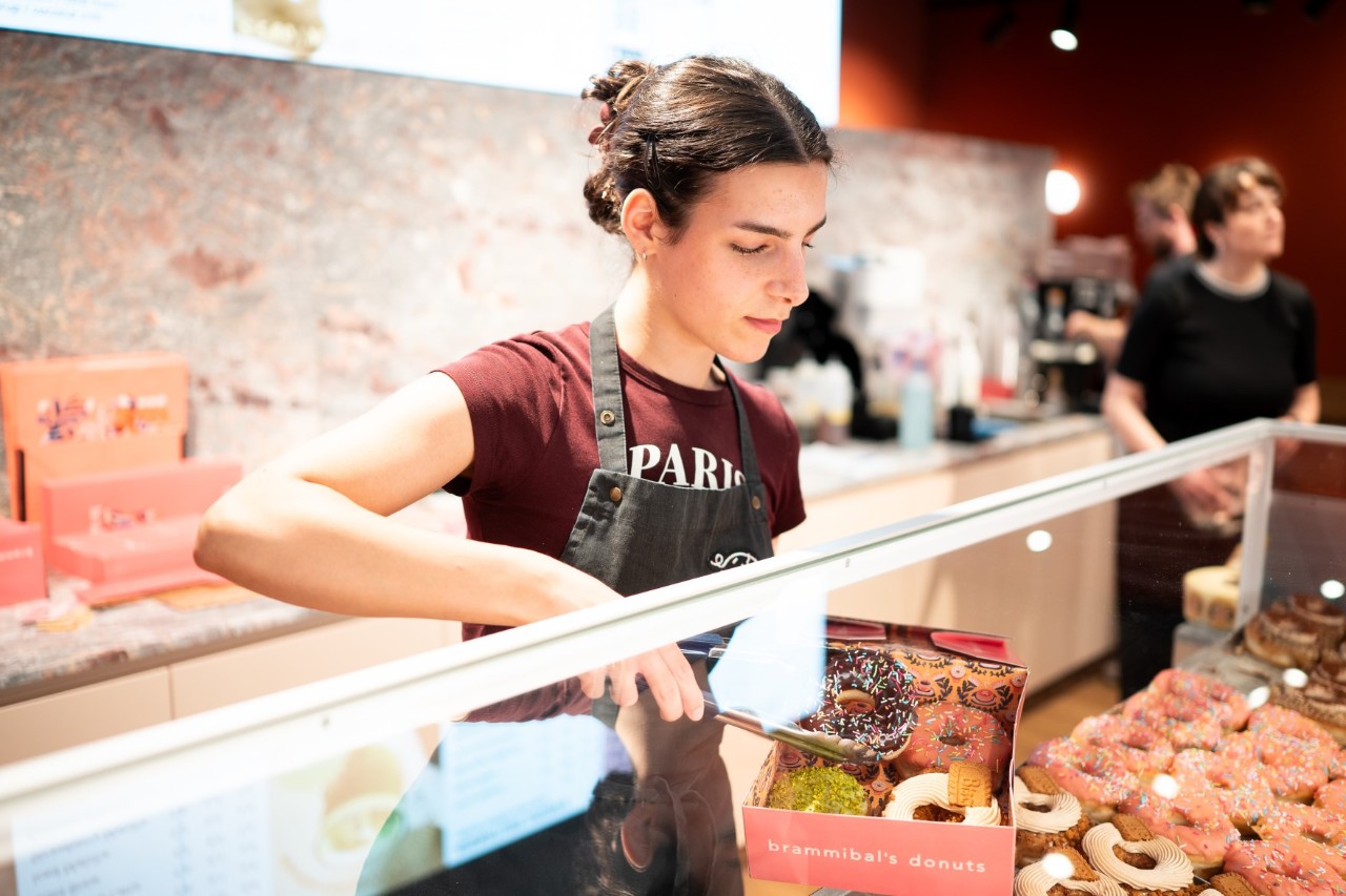 A shop assistant at a counter displaying doughnuts.