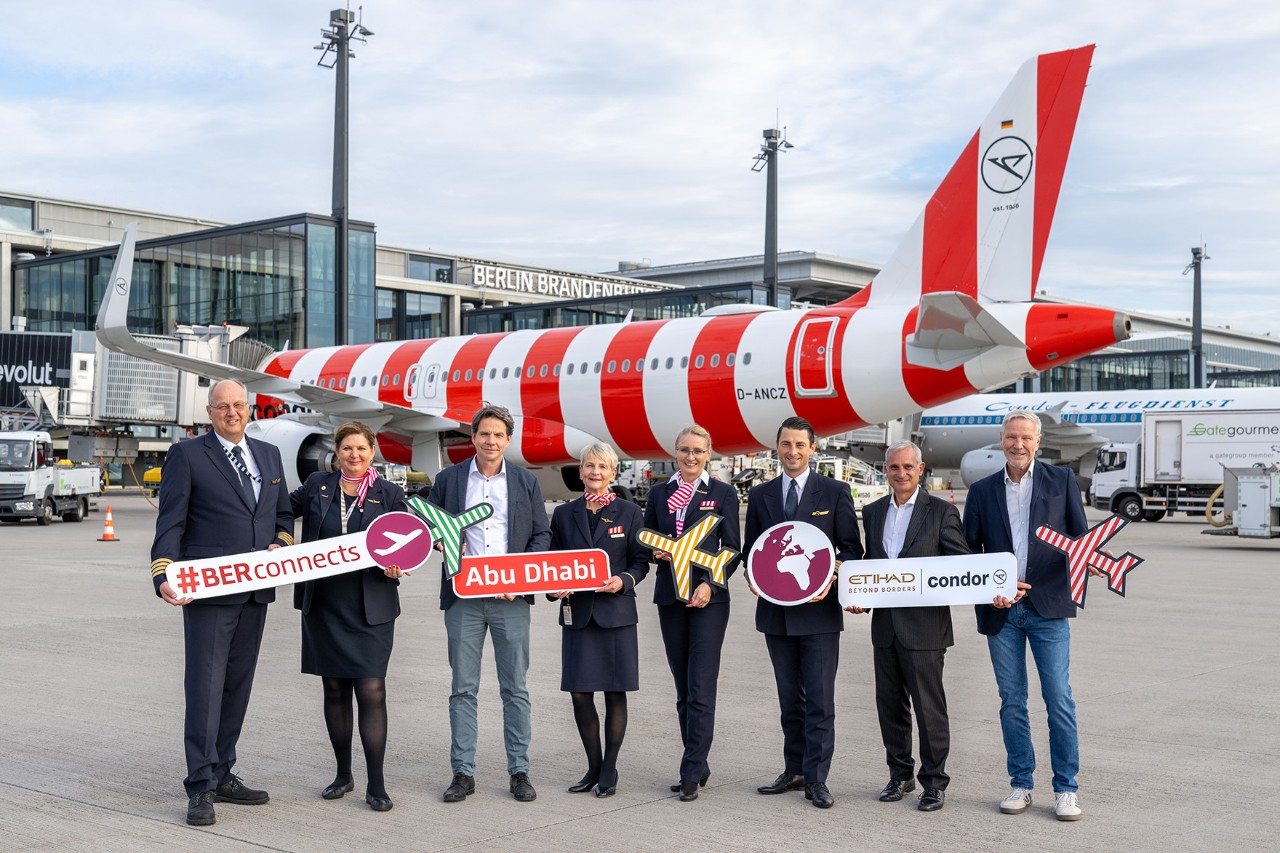 A group of people holding signs in front of a Condor aircraft at BER