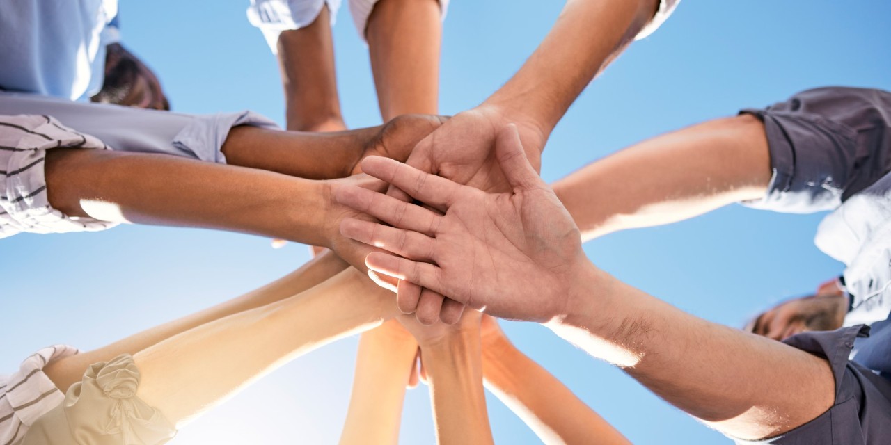 You can see the hands of a group of people, who are standing in a circle, stacked on top of each other.
