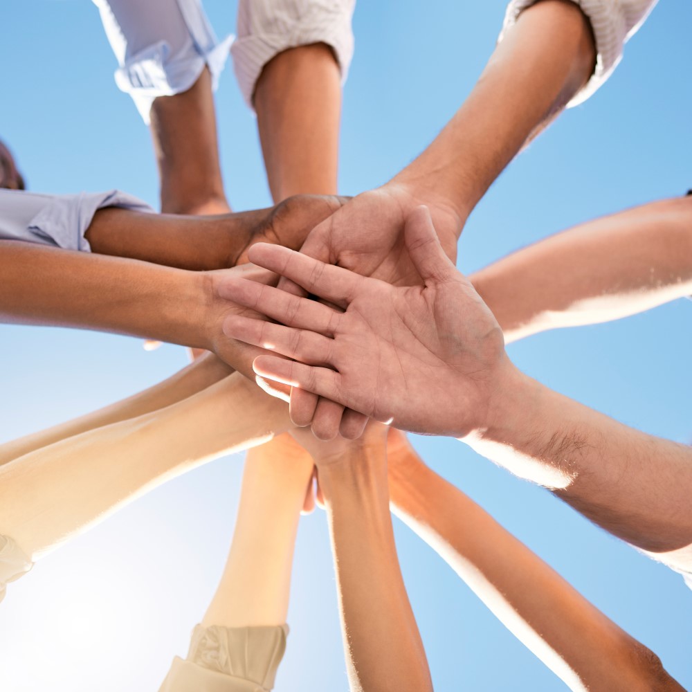 You can see the hands of a group of people, who are standing in a circle, stacked on top of each other.