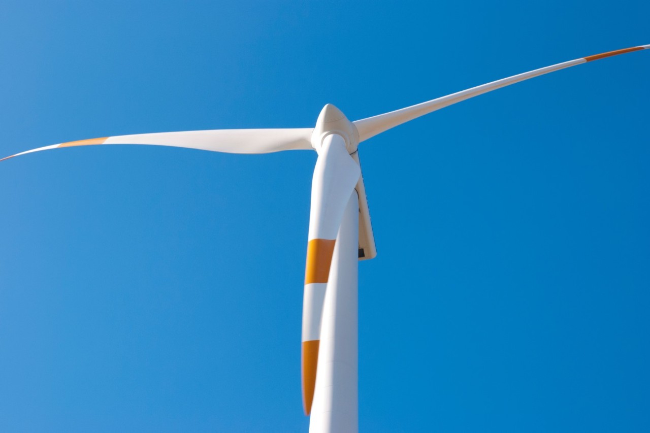 A wind turbine with white and orange blades and a blue sky in the background