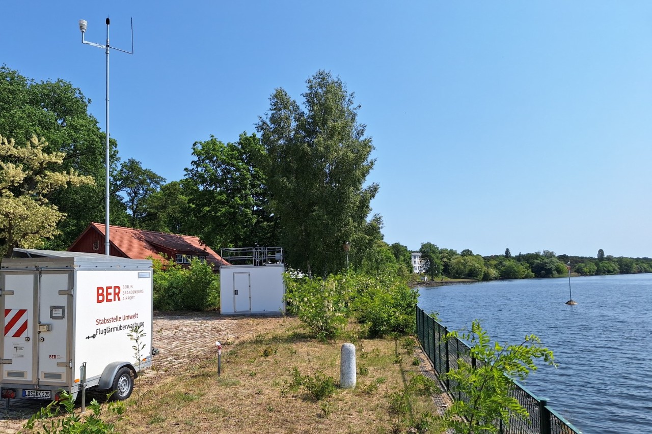 A mobile aircraft noise measurement trailer is parked on the shore of a lake.