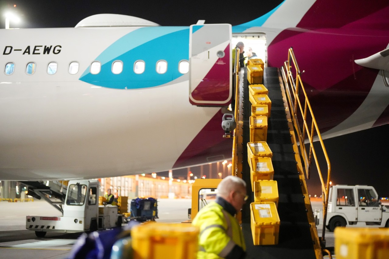 Yellow post boxes are loaded onto an aircraft via a conveyor belt.