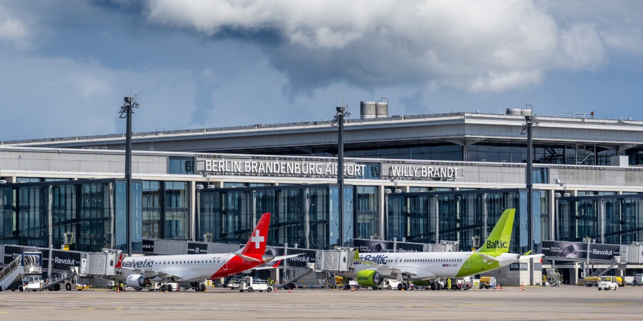 Two planes, one Swiss and one Air Baltic, are parked in front of Terminal 1. Above them is a large cloud.